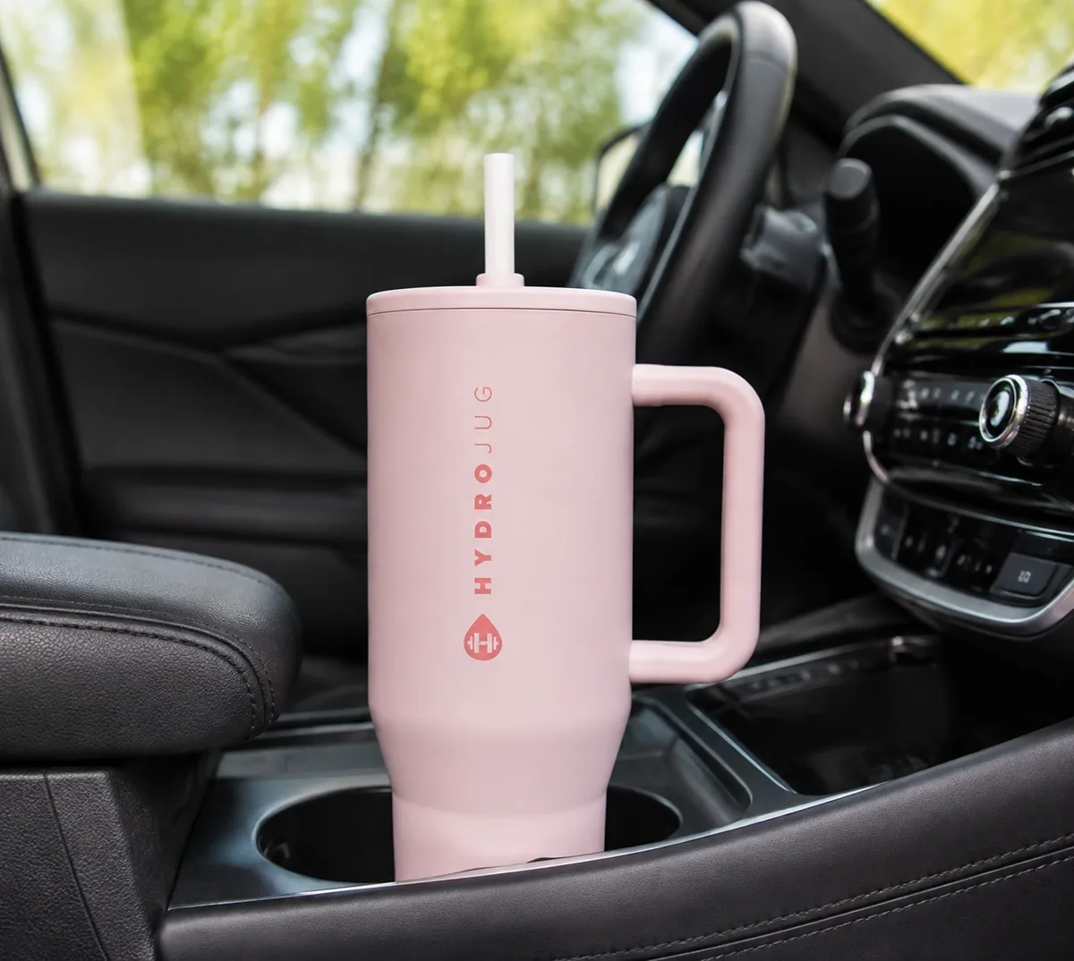 HydroJug Traveler 40oz tumbler in Pink Sand with handle and flip straw, shown on a car cup holder.